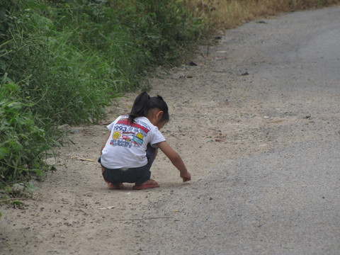 乡村道路边捡石子的女孩