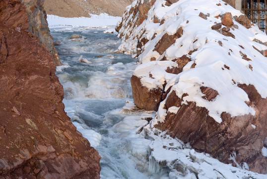 红色山崖挟持的冰雪溪流