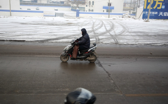 下雪天马路上骑电动车的人