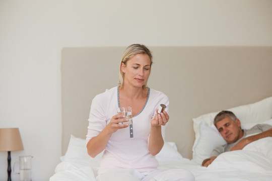 坐在床上吃药的妻子和她的丈夫