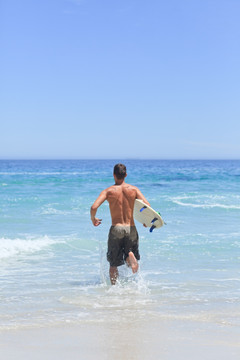 在沙滩上拿着冲浪板奔跑的男人