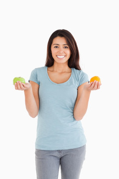 女人拿着一个苹果和一个橘子