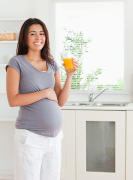 孕妇站在厨房里拿着橙汁