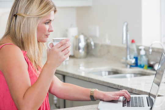 边喝咖啡边使用笔记本电脑的女人