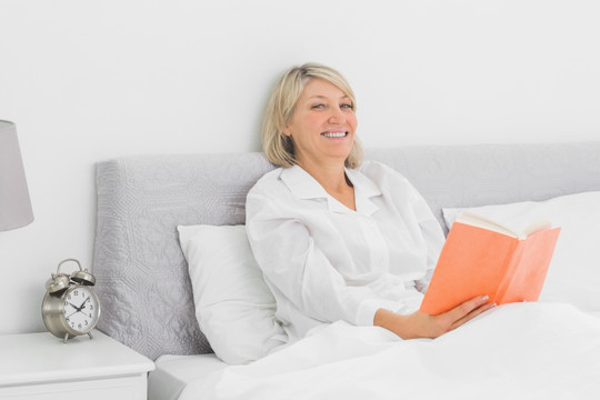 快乐的女人坐在床上看书