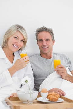 在床上吃早餐喝橙汁的夫妇