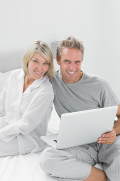 夫妇使用笔记本电脑坐在床上