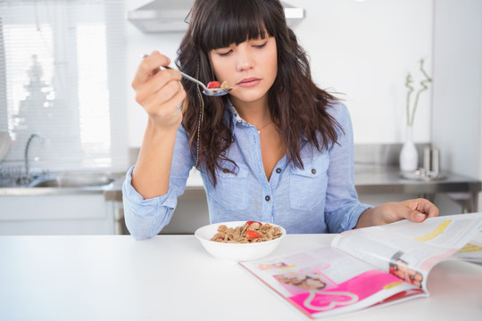 在吃麦片阅读杂志的女人