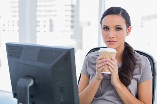 坐在办公室拿着一杯咖啡的女人