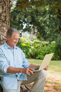 坐在树干上用笔记本电脑的老人