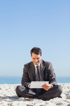 坐在沙滩上使用平板电脑的男人