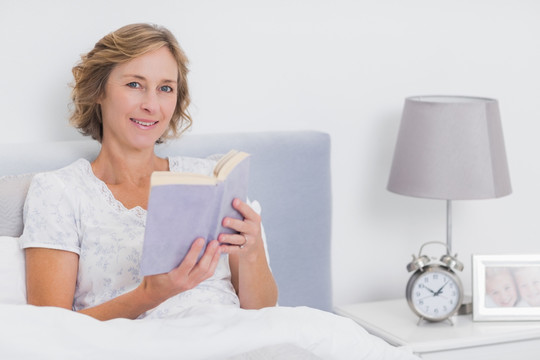 快乐的金发女子坐在床上看书书