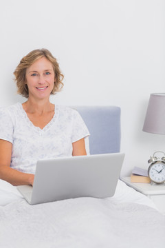 微笑的女人坐在床上用笔记本电脑