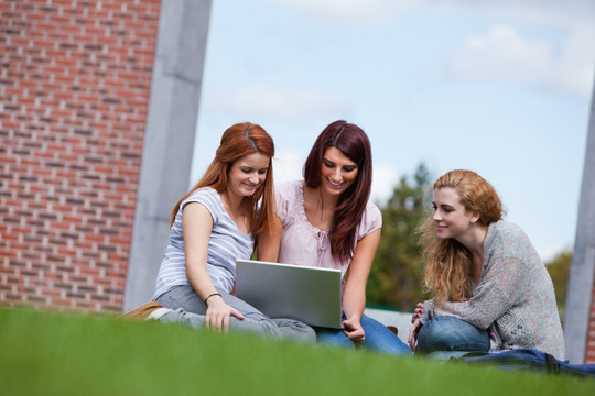 坐在草坪上使用电脑的大学生们