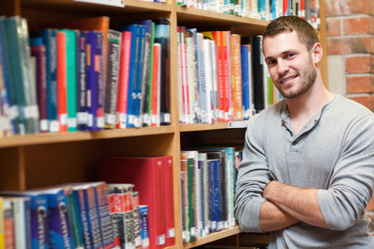 微笑的男生抱着双臂在图书馆里