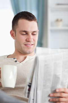 男人坐沙发上手拿杯子看报纸