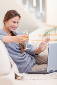 用电脑的女人手拿一杯白葡萄酒