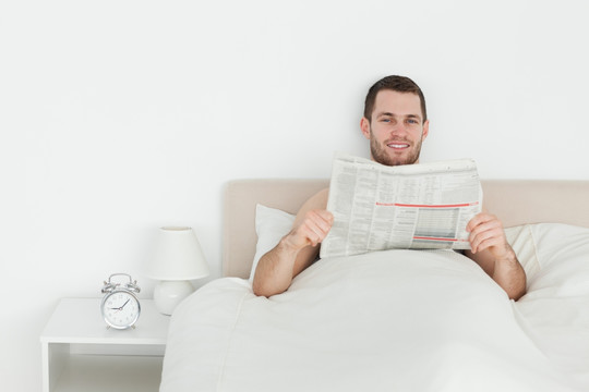 微笑的男人在他的卧室里看报纸