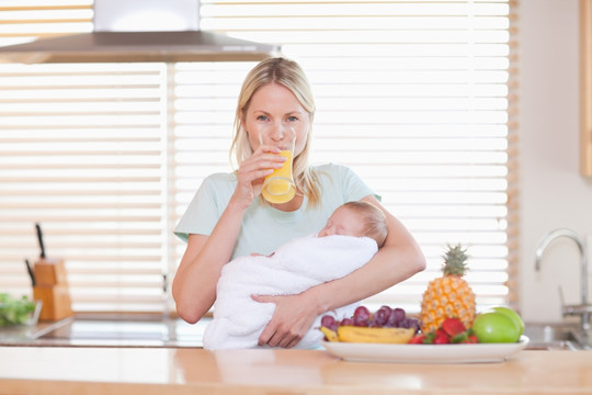 在厨房抱着婴儿喝橙汁的女人