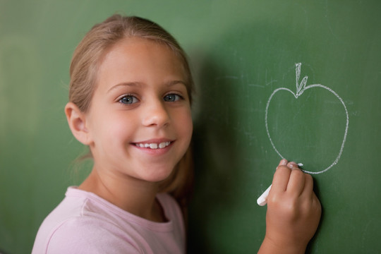 微笑的女学生在黑板上画一个苹果