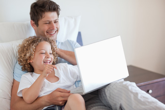 父亲和孩子在床上使用笔记本电脑