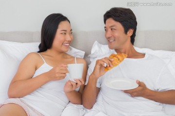 夫妇躺在床上微笑着吃着早餐