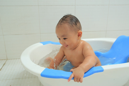 胖胖婴儿坐洗澡盆里快乐的玩水