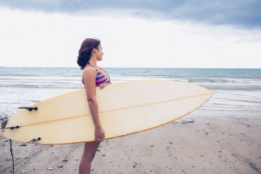 站在海滩上拿着冲浪板的女人