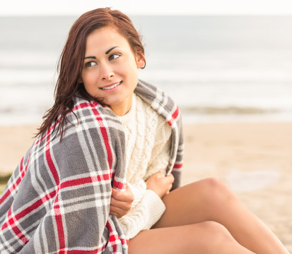 披着毯子坐在海边的女人