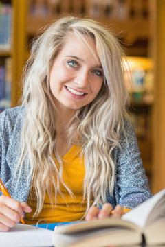 微笑的女学生坐在图书馆的桌子前