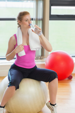 坐在健身球上喝水的女人