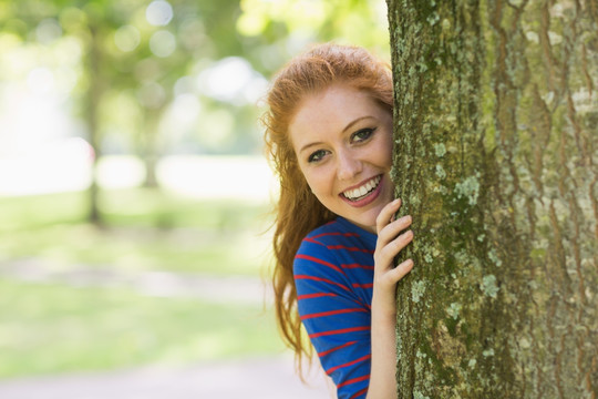 微笑的女大学生躲在树后面