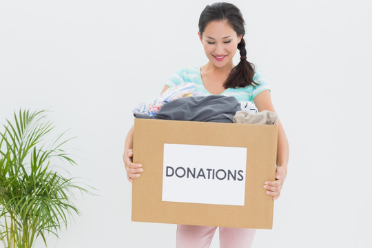 微笑的年轻女人抱着一箱募捐衣服