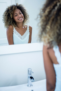 微笑的女人在浴室里看着镜子