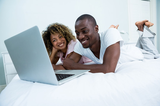 躺在床上使用笔记本电脑的夫妇