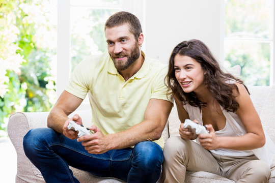 一对年轻夫妇坐在沙发上玩游戏机