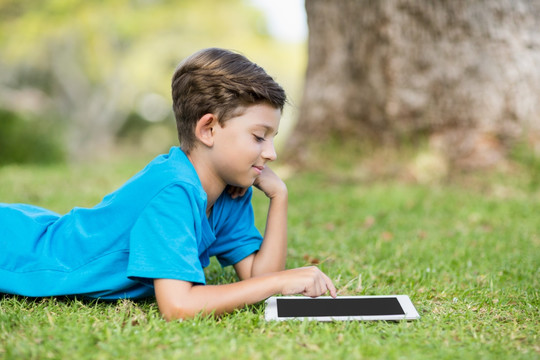 趴在草地上使用平板电脑的小男孩