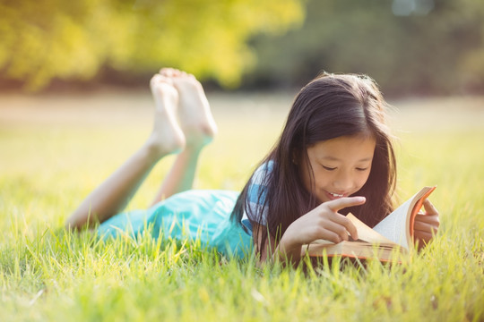 微笑的女孩躺在草地上看书