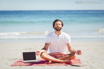 盘着腿坐在海滩上练习瑜伽的男人