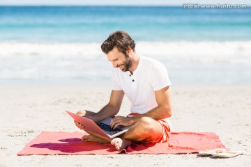 盘腿坐在沙滩上用电脑的男人