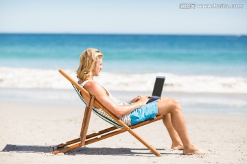 坐在沙滩椅上用笔记本电脑的男人