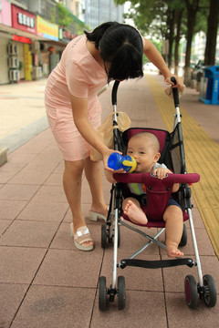 妈妈给婴儿车上的宝宝喂水