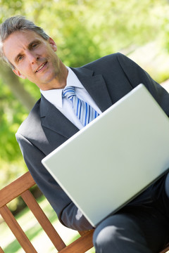 坐在长椅上用笔记本电脑的男人