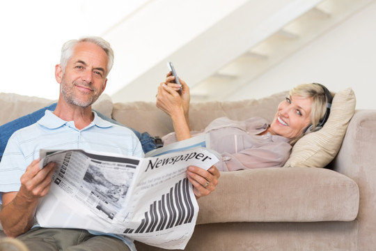 在客厅里看报纸和用手机的夫妇