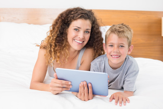 母亲和儿子坐在床上用平板电脑