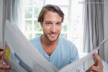 微笑的男人坐在床上看报纸