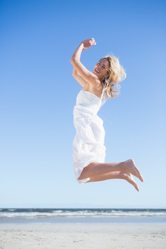 穿着白裙在沙滩上跳跃的女人