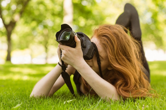趴在草坪上拿着相机拍照的女人