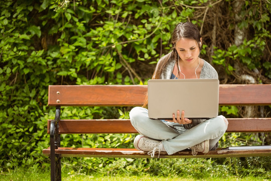 坐在长椅上用笔记本电脑的女学生