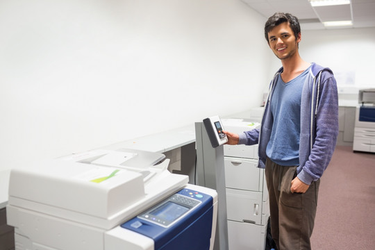 微笑的男大学生站在复印机前